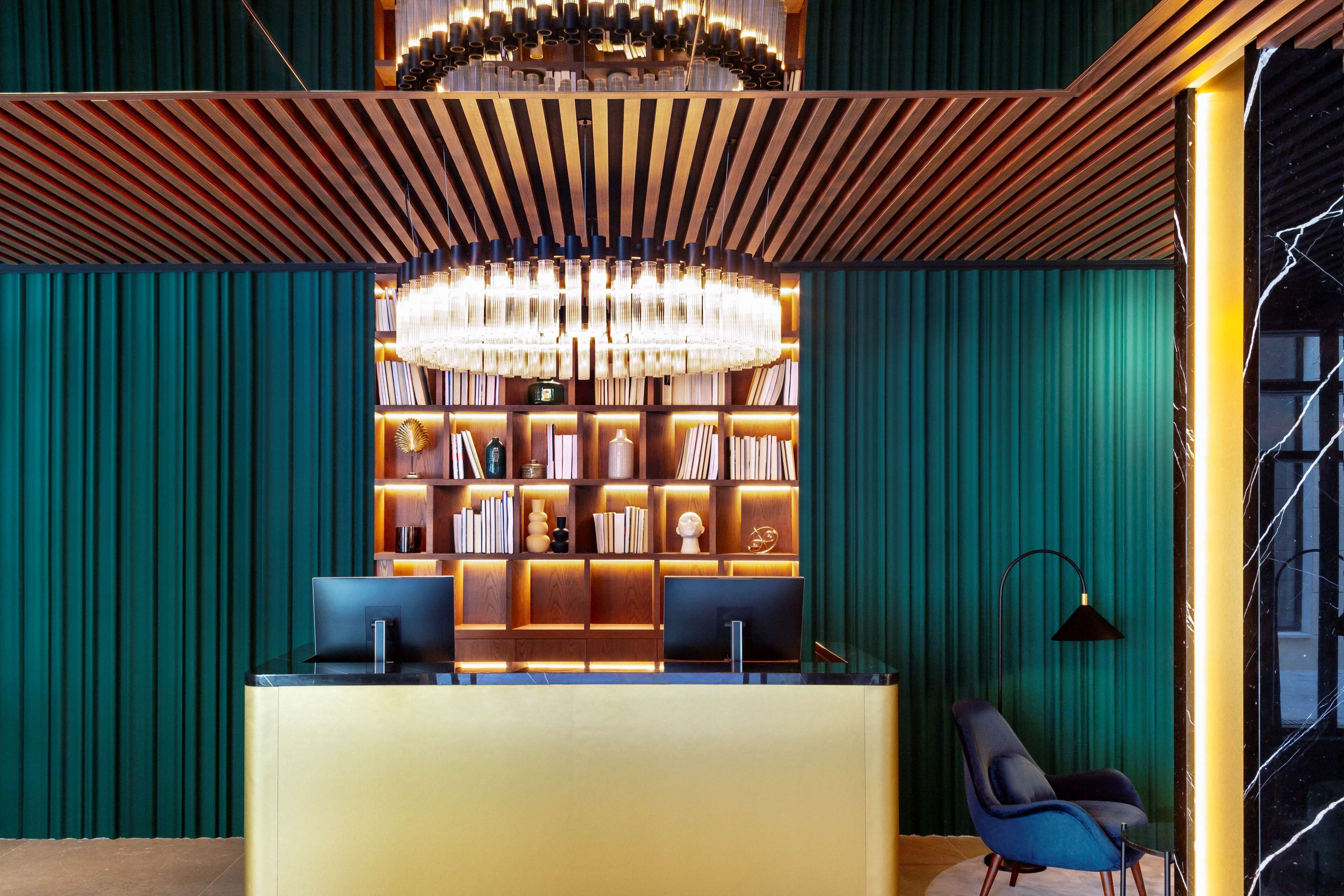 A reception area with a desk, two computer monitors, a chandelier, and a bookshelf.