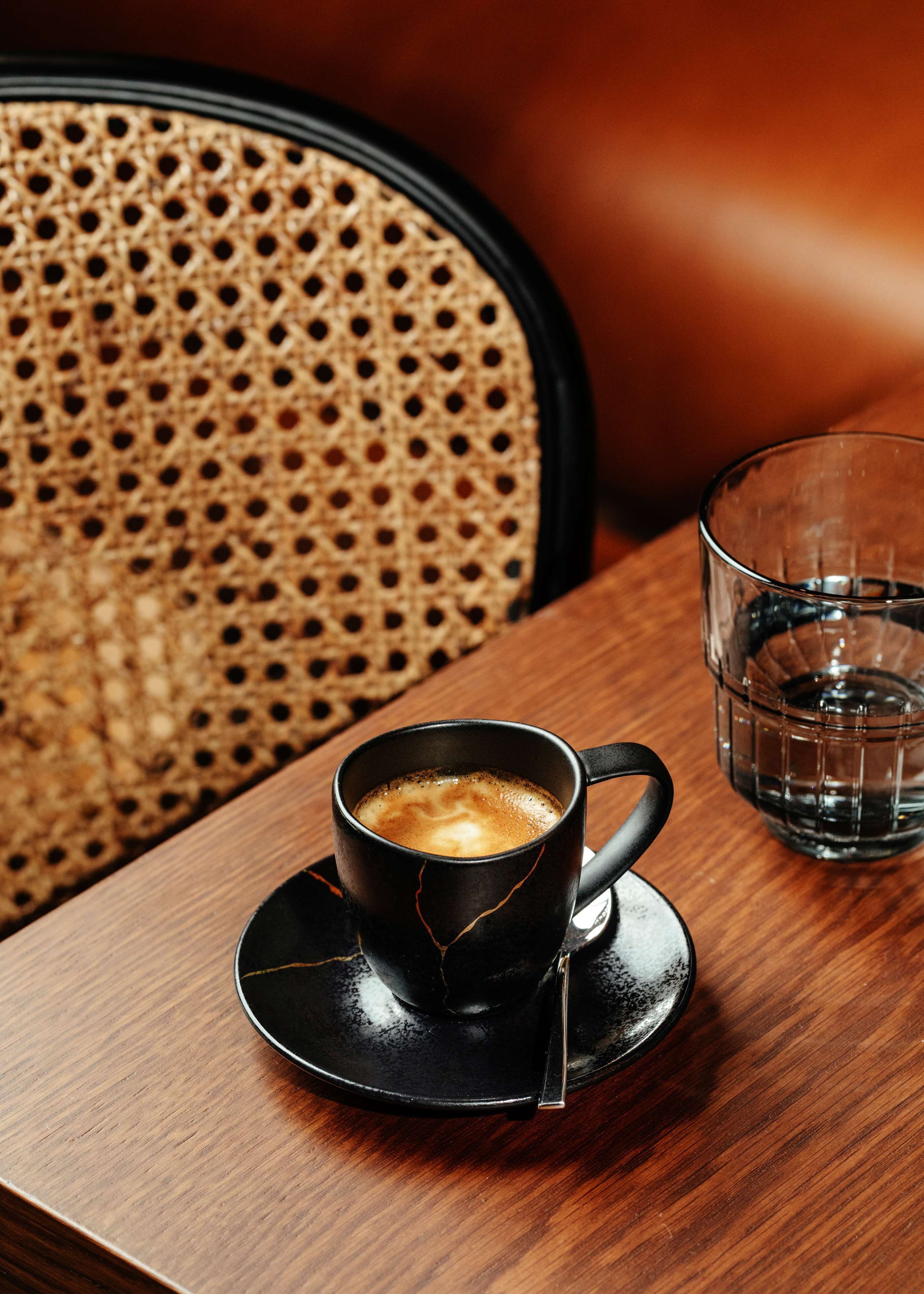 Une tasse de café noir, posée sur une soucoupe, sur une table en bois.