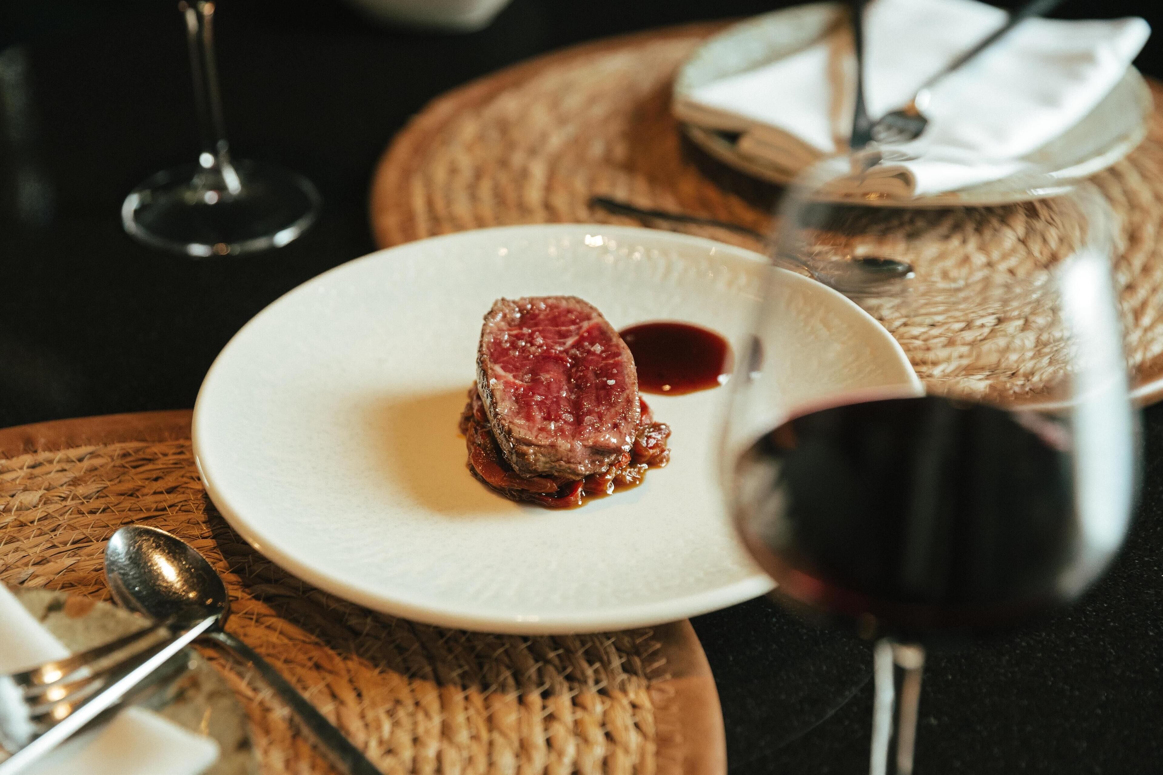 Een bord met steak, saus en een glas rode wijn, op een geweven placemat.