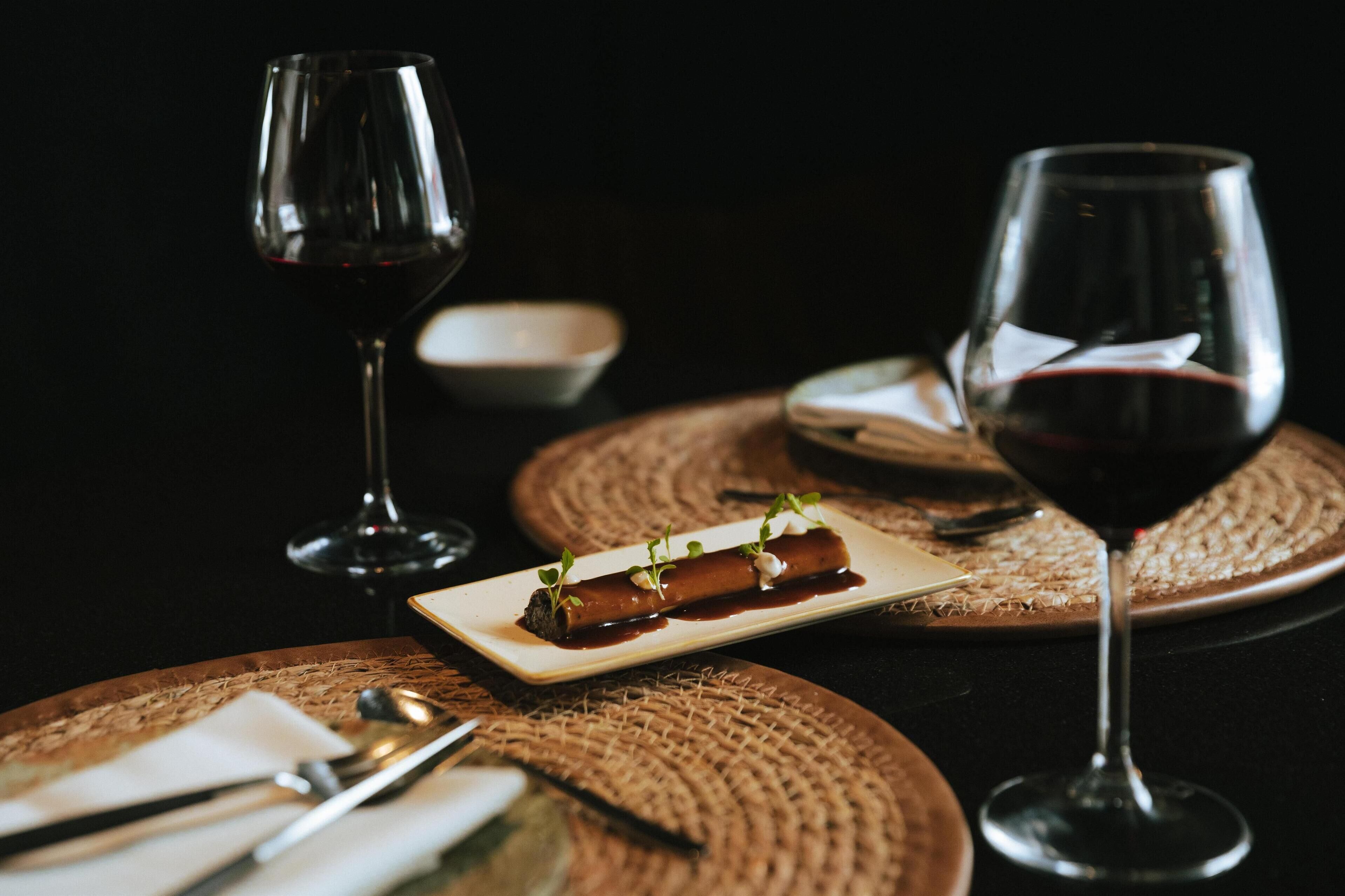 Una mesa de comedor con un plato de comida, dos copas de vino y cubiertos.