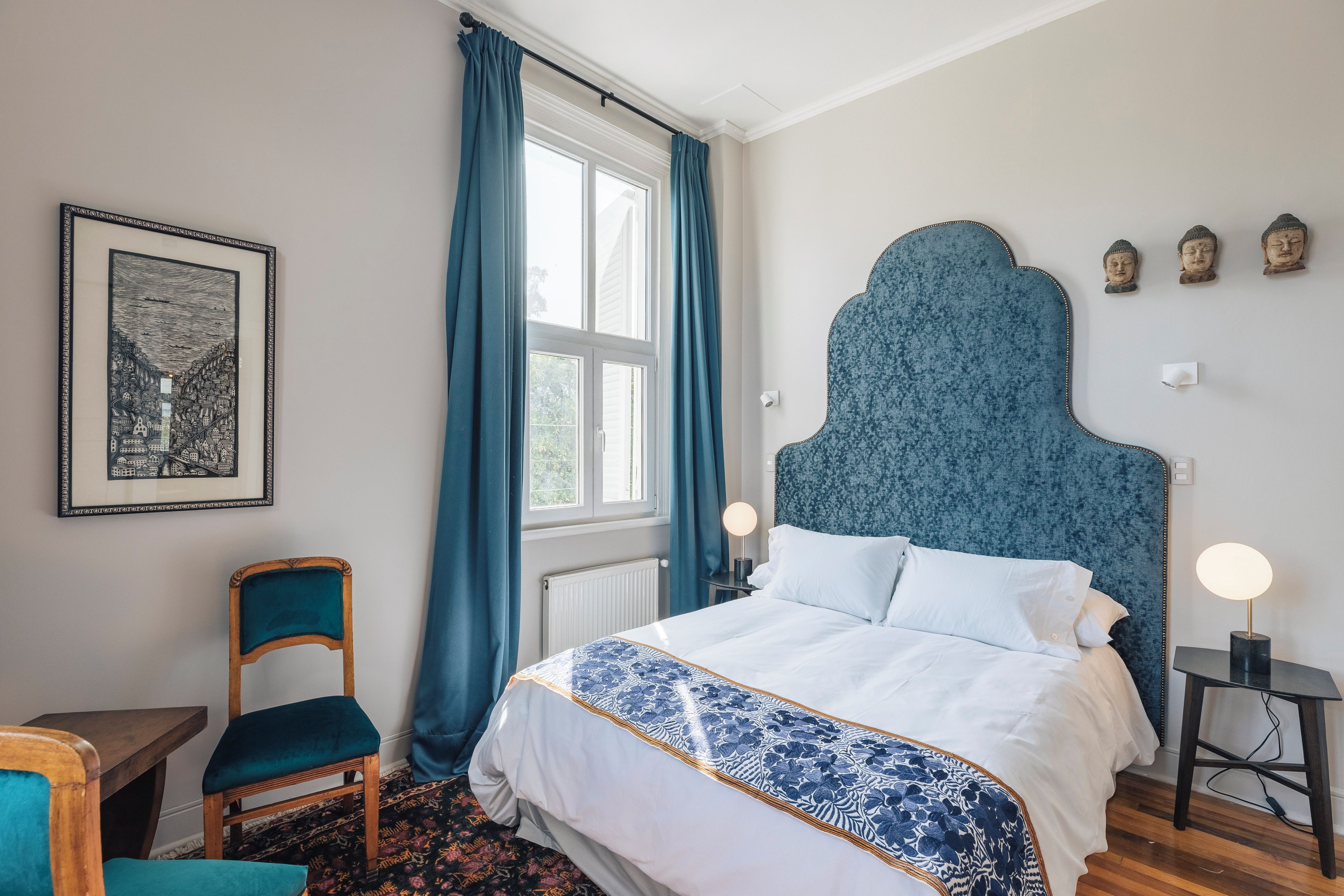 A bedroom with a bed, a chair, a table, and a window with curtains.
