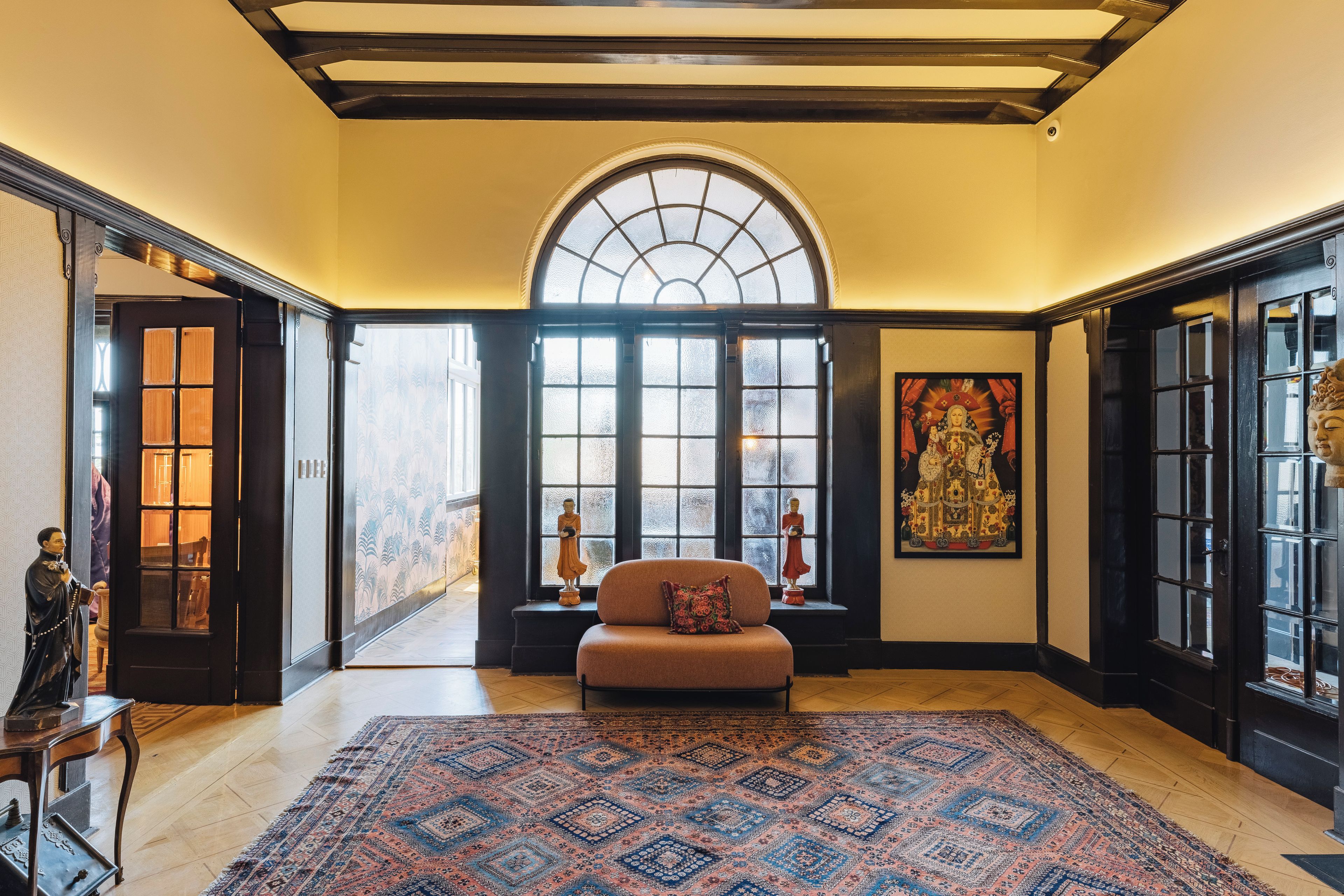 A spacious room with a large window, a sofa, a patterned rug, and a Buddha statue.