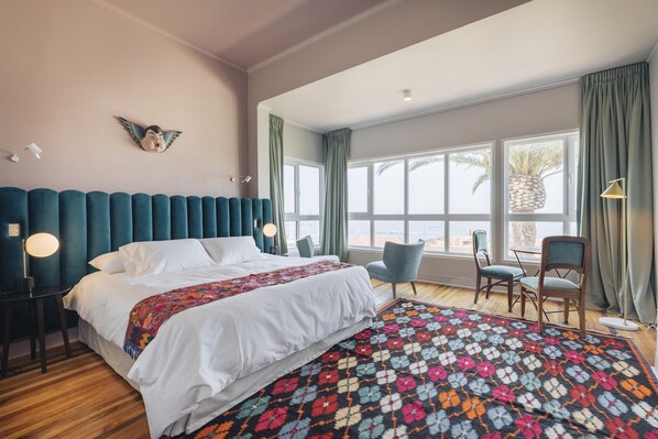 A bedroom with a large bed, a colorful rug, and a view of palm trees through the window.