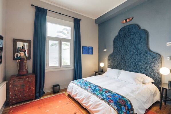 Une chambre à coucher comprenant un lit, une table de chevet, une commode, une fenêtre avec des rideaux et une tête de lit.