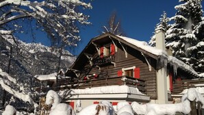 Una cabaña de madera con balcón, rodeada de árboles cubiertos de nieve y un cielo azul despejado.