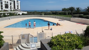 En swimmingpool med havudsigt, omgivet af et hvidt hegn og grønt vegetation.