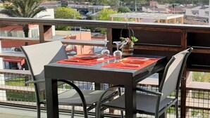 En balkon med et bord dækket til to, med udsigt over et boligområde med huse og grønne områder.