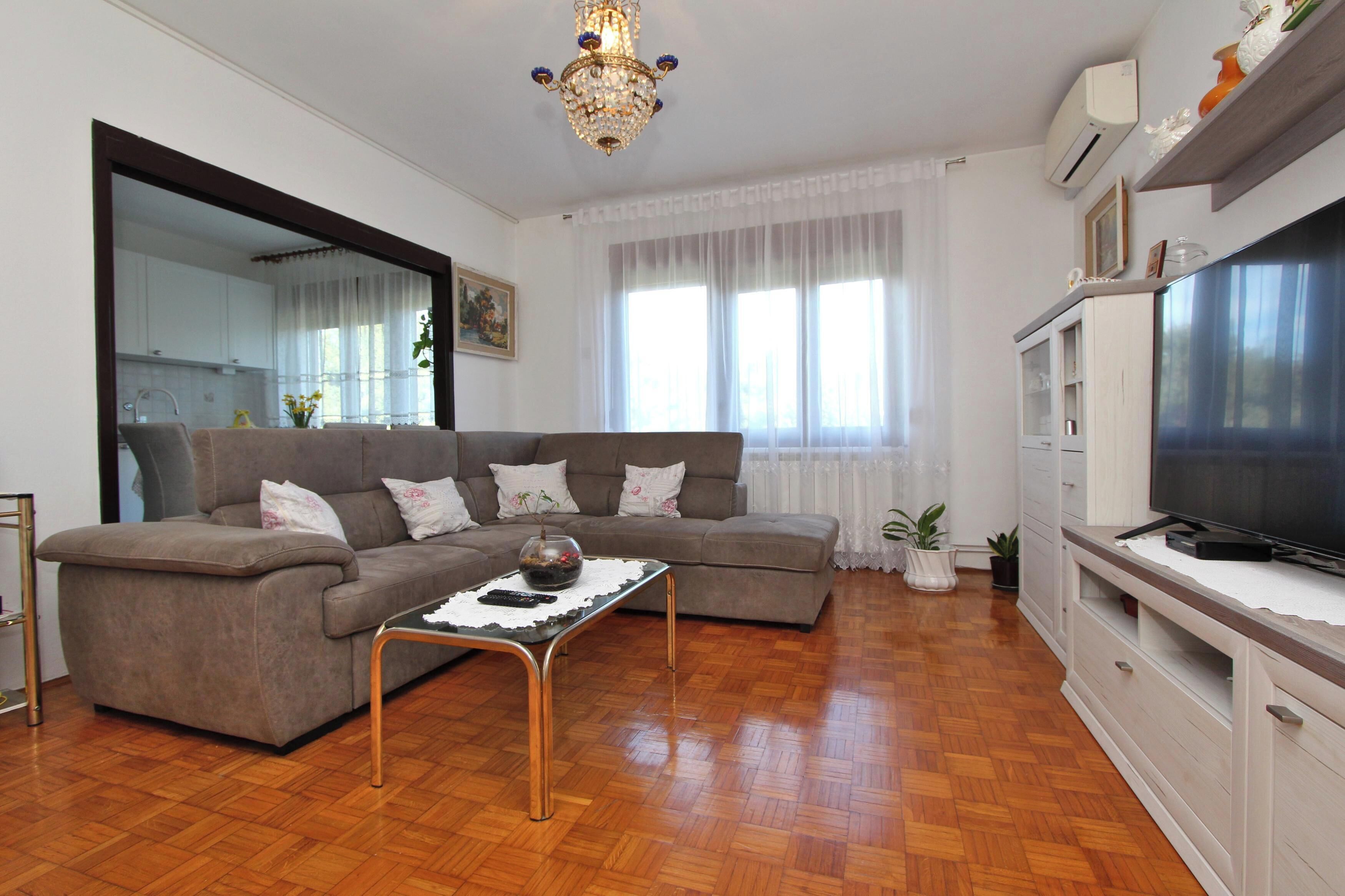 A living room with a sofa, a coffee table, a TV, and a chandelier.