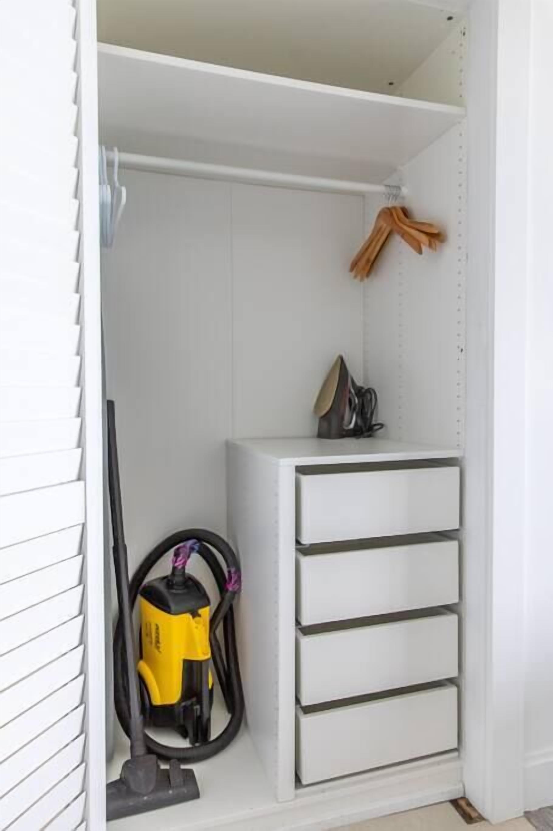 A white closet with a vacuum cleaner and a pair of shoes on the top shelf.