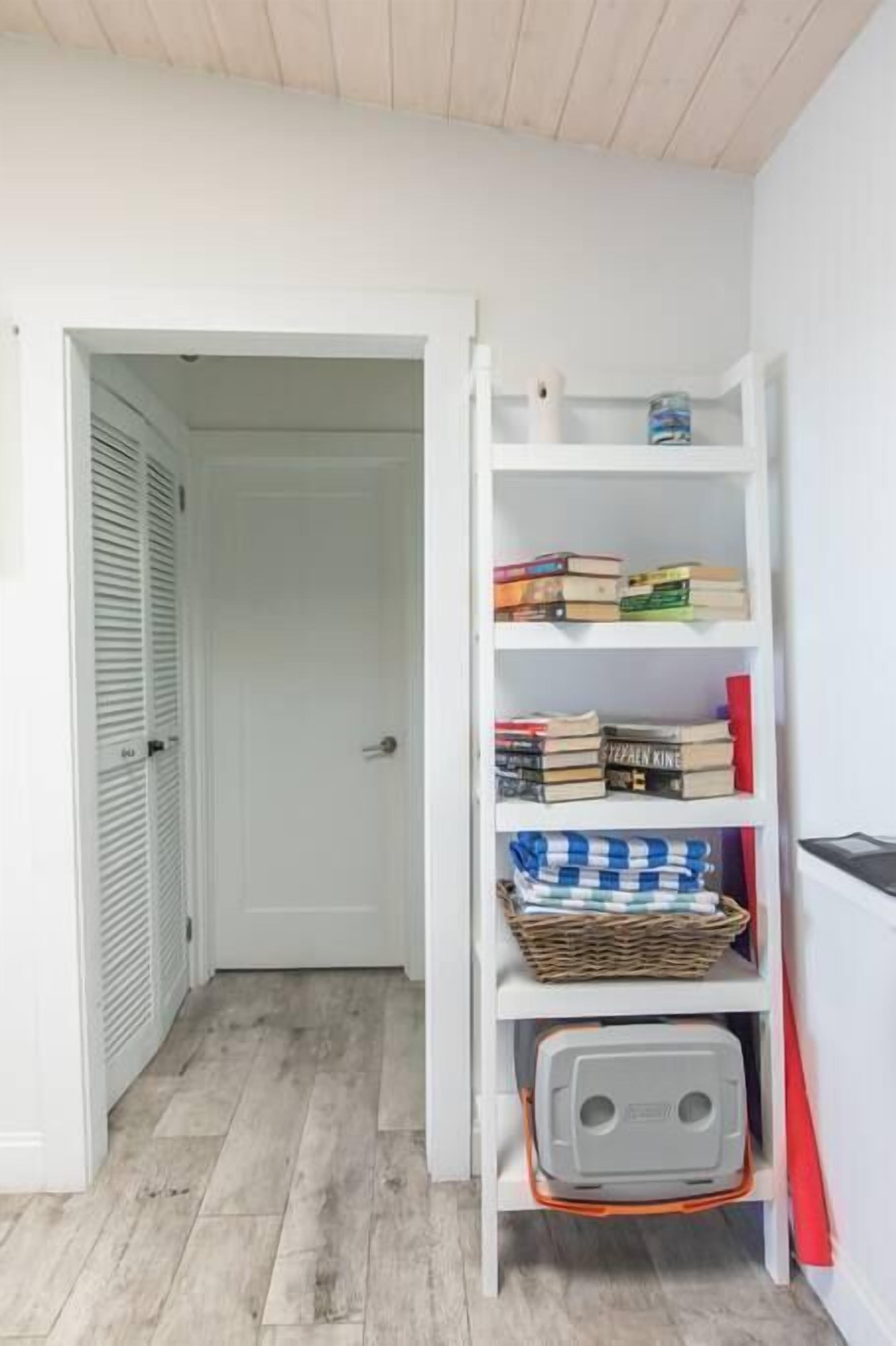 Een witte boekenkast met boeken en een mand, een gesloten deur, en een houten vloer.