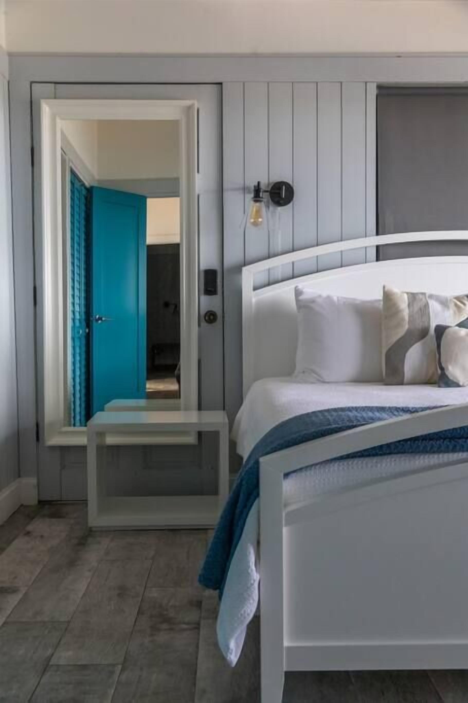 Ein Schlafzimmer mit einem weißen Bett, einer blauen Tür und einer Wandleuchte.