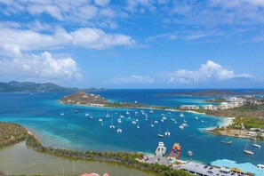 A coastal marina with numerous boats, a small island with buildings, and a clear blue sky.