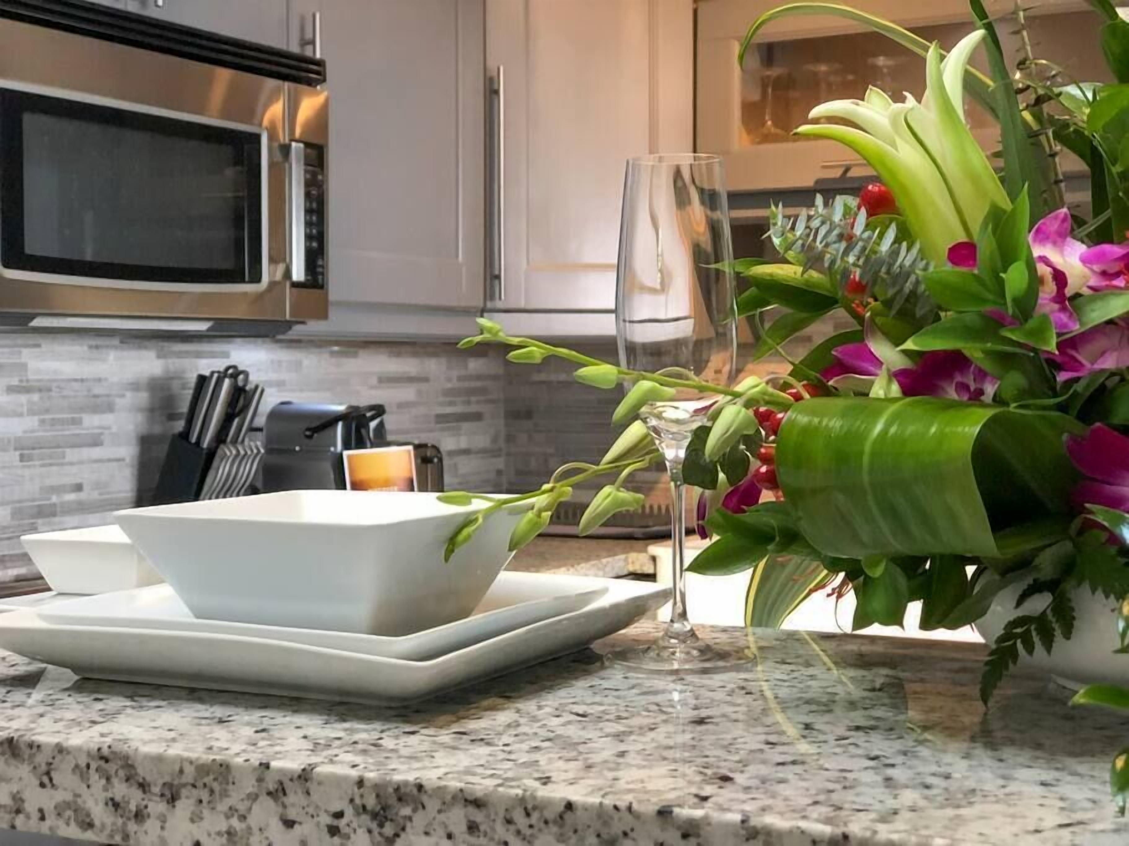 Un comptoir de cuisine avec un saladier blanc, un verre et un vase rempli de fleurs.