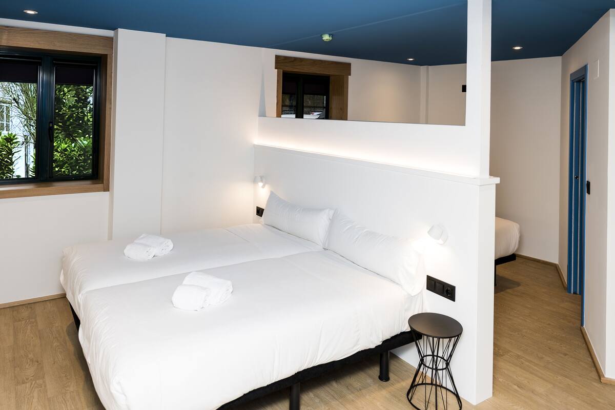 Habitación de hotel moderna con una cama grande, una mesita redonda y una ventana con vistas a zonas verdes.