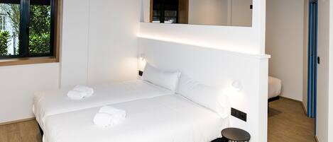 Habitación de hotel moderna con una cama grande, una mesita redonda y una ventana con vistas a zonas verdes.
