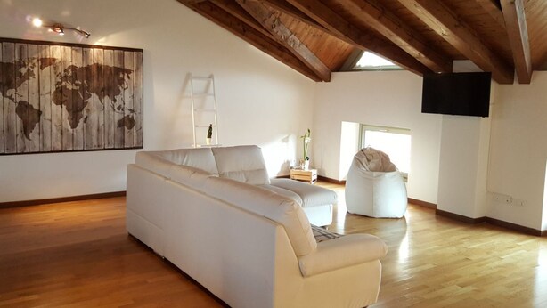 Ein geräumiges Wohnzimmer mit hohen Holzbalken, einer großen Weltkarte als Bild, einem weißen Sofa, einem Sitzsack und einem flachbildfernseher an der Wand.