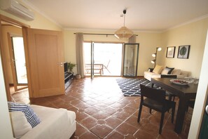 Un salon comprenant un canapé, une table à manger et des chaises, une porte-fenêtre coulissante donnant sur un balcon et un ventilateur de plafond.