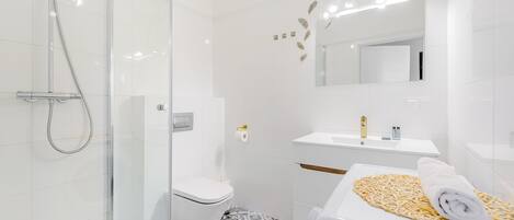 A modern bathroom with a glass shower enclosure, a toilet, a sink with a mirror, and a towel on the toilet.