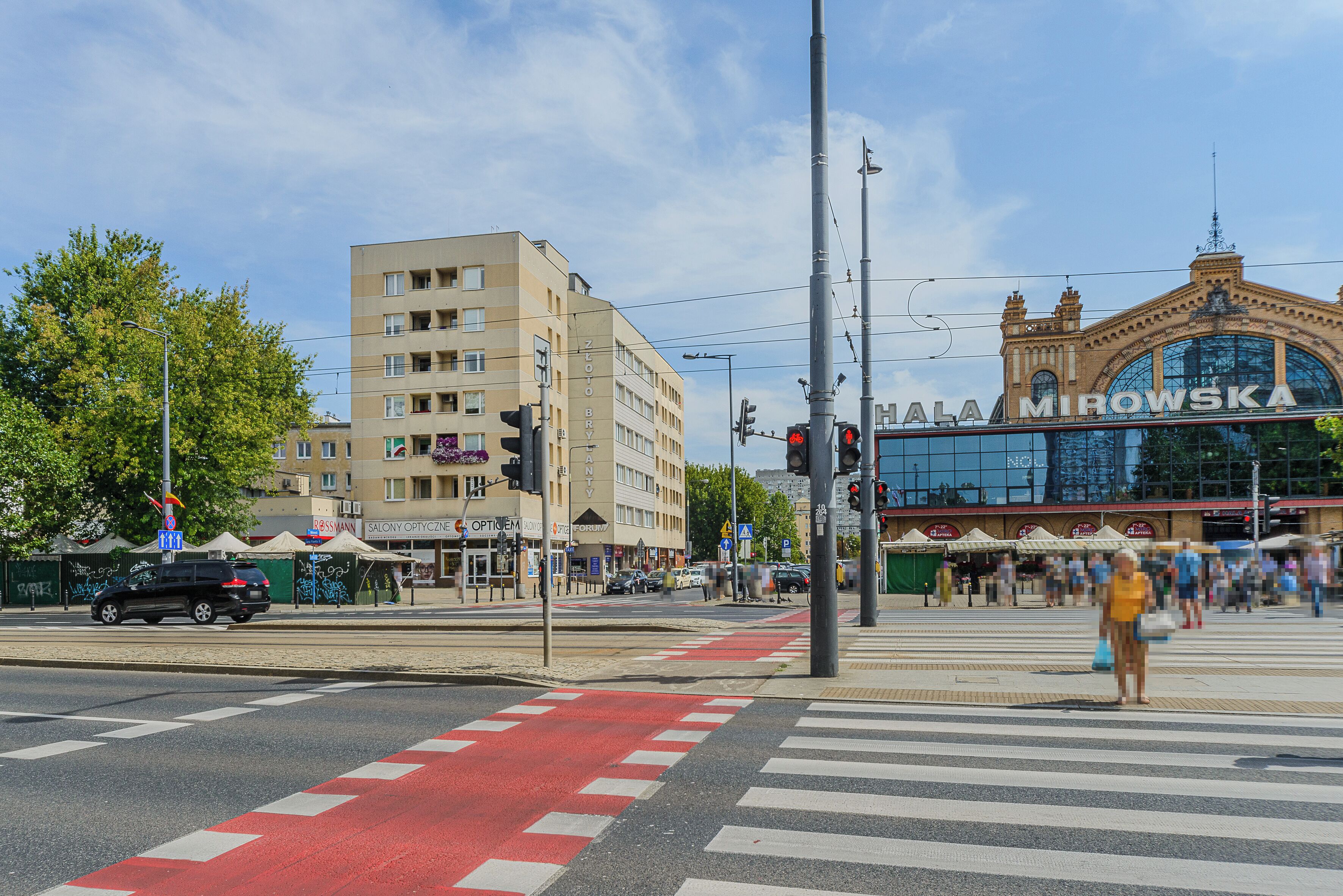 A street intersection with a tram line, a building with a sign reading "HALA MIROWSKA", and a pedestrian crossing.