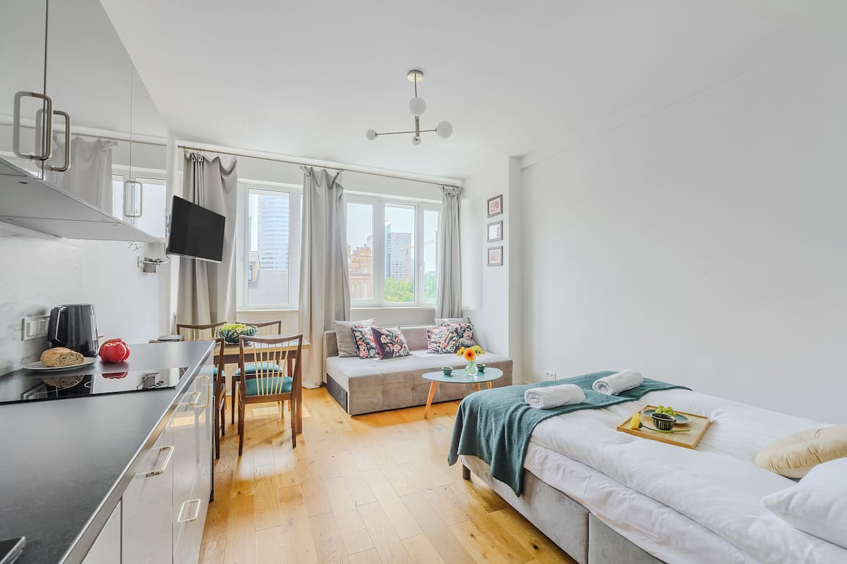 Ein modernes, helles Zimmer mit Küchenzeile, Esstisch, Sofa und Bett.