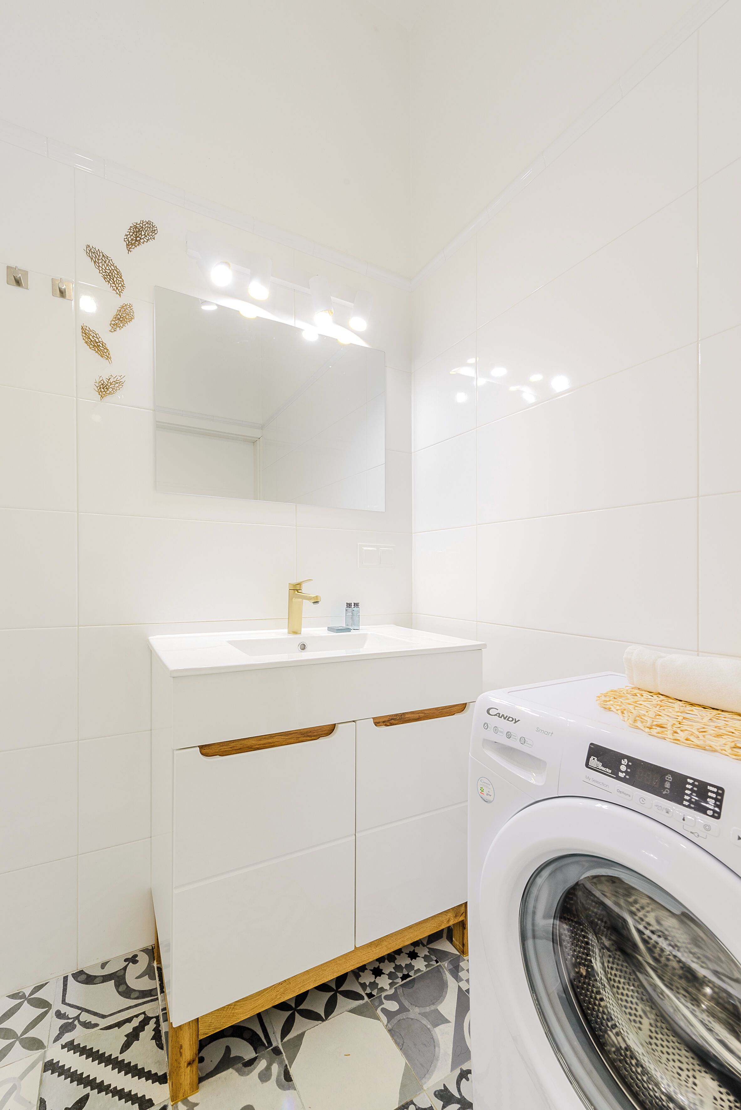 A modern bathroom with a white sink, gold faucet, and a washing machine.