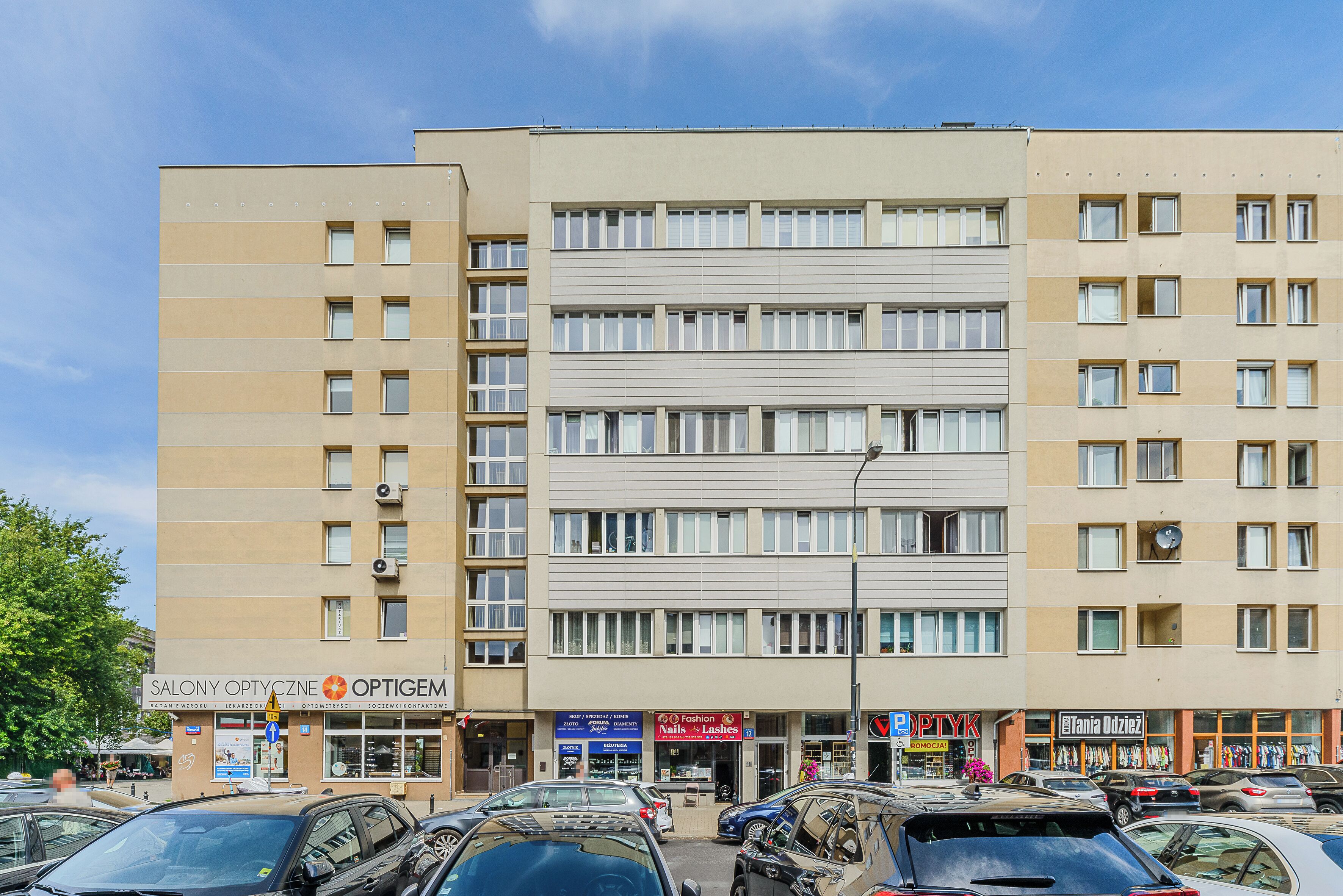 A multi-story building with various commercial establishments on the ground floor, including a salon and a nail shop.
