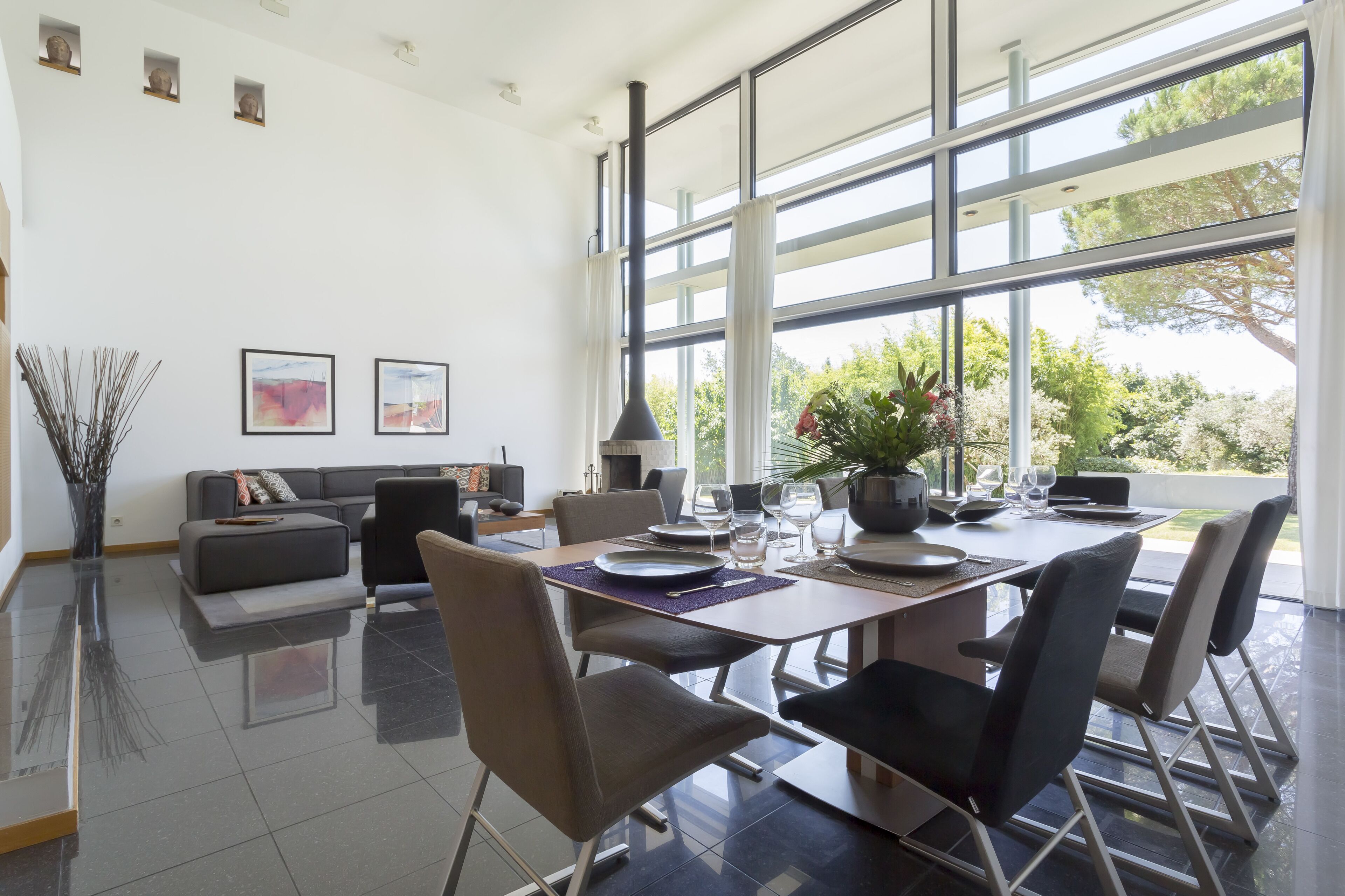 Un comedor moderno con un ventanal grande, un sofá y una mesa de comedor preparada para seis comensales.