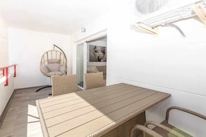 Un balcón con una mesa de madera, sillas de mimbre, una silla colgante y un ventilador fijado a la pared.