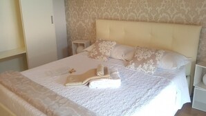 Un lit bien fait, avec une couvre-lit à motifs et des oreillers, une table de chevet avec une lampe, et une armoire en arrière-plan.
