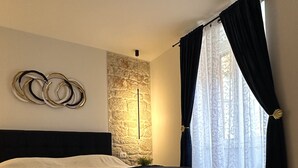 Un dormitorio con cama, pared de piedra, lámpara colgante y ventana con cortinas.