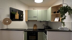 Cocina compacta con una isla central, una planta colgante y un panel de tacos con utensilios de cocina.