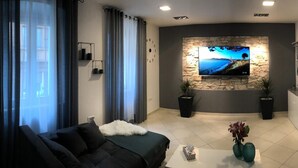 A modern living room with a large flat-screen TV mounted on a stone wall, a sofa, a coffee table with a vase, and a potted plant. - Apartment Porta Aurea (Pula)