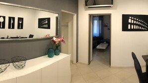 A modern interior with a white reception desk, a large mirror, and black wall art. - Apartment Porta Aurea (Pula)