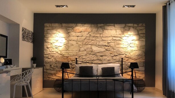 A bedroom with a stone wall, a bed with black headboards, a desk, and a chair. - Apartment Porta Aurea (Pula)