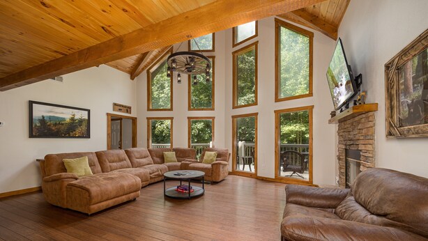 A spacious living room with a large sectional sofa, a round coffee table, and a fireplace. - Secluded Smoky Mountain Cabin with Private Waterfall, Creek, & Luxury Amenities! (Sevierville)