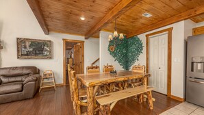 A rustic dining area with a wooden table and benches, a leather couch, and a refrigerator. - Secluded Smoky Mountain Cabin with Private Waterfall, Creek, & Luxury Amenities! (Sevierville)