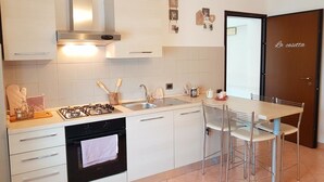 Une cuisine moderne avec des meubles blancs, une cuisinière à gaz, un évier et un coin repas comprenant une table et des chaises.