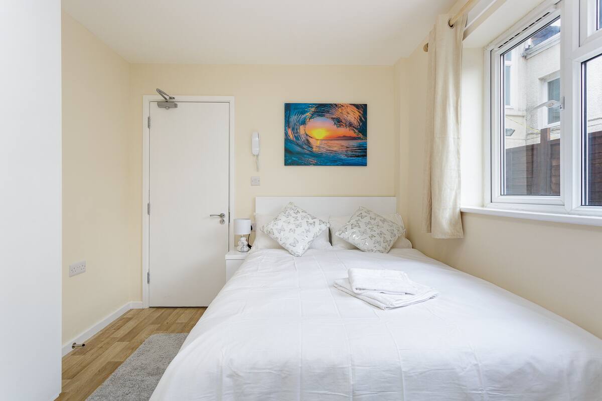 A bedroom with a bed, a painting, a window, and a door.