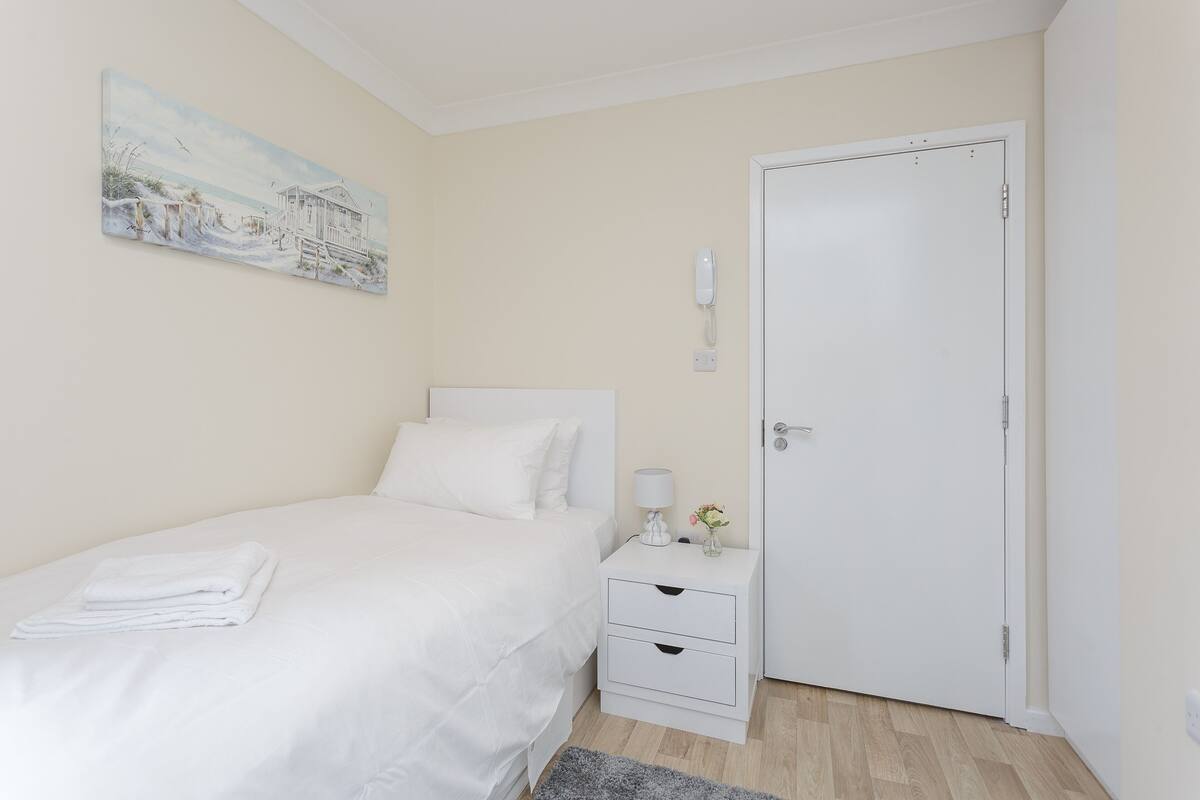 A bedroom with a bed, a nightstand, a door, and a painting on the wall.