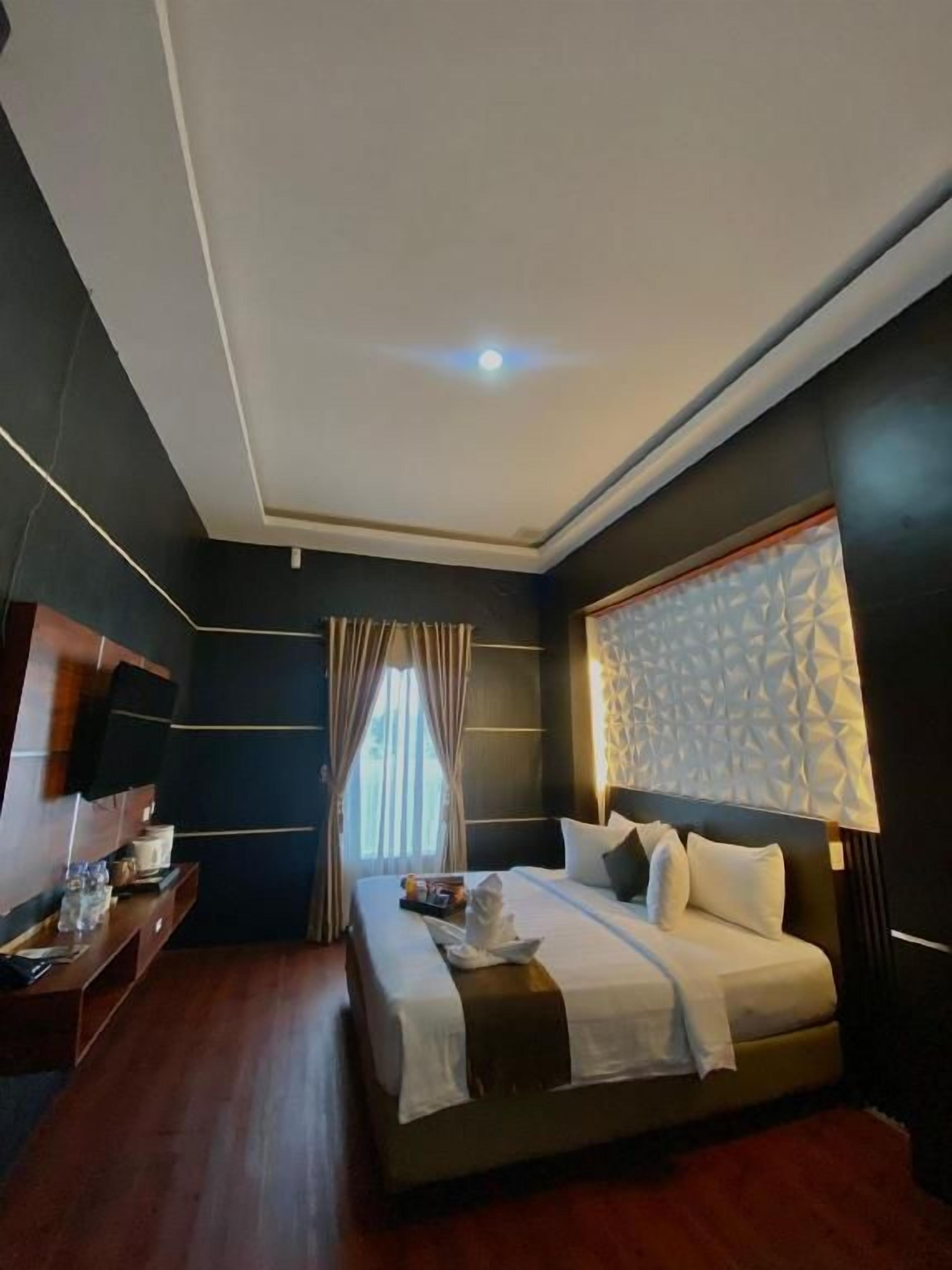 A modern hotel room with a large bed, a flat-screen TV, and a window with curtains.