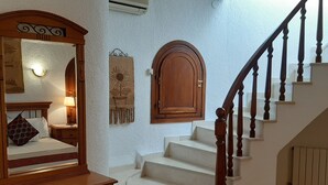 Un dormitorio con un espejo grande, una mesita de noche, un cabecero de madera, una lámpara, una obra de arte en la pared y una escalera con barandillas de madera.
