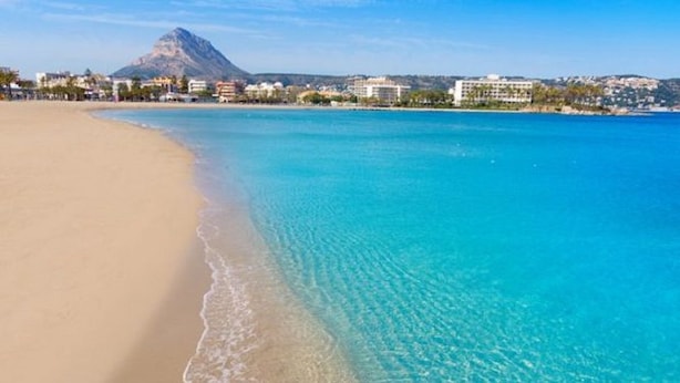Una playa con aguas turquesas cristalinas, una orilla arenosa y una montaña al fondo.