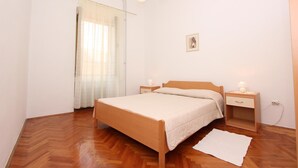 A bedroom with a wooden bed, two bedside tables with lamps, a white rug, and a window with sheer curtains. - Apartment Riki (Rovinj)