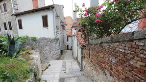 A narrow stone pathway flanked by a brick wall and a white building with a tiled roof. - Apartment Riki (Rovinj)