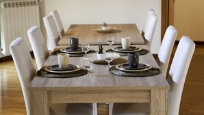 Une table à manger, avec des chaises blanches, de l’assiette, des couverts et de la verrerie.