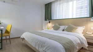 Habitación de hotel con cama, escritorio, silla, mesita de noche y ventana con cortinas.