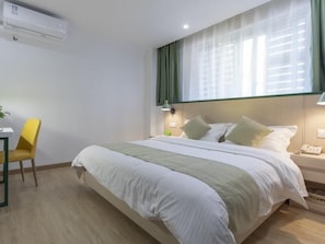 Habitación de hotel con cama, escritorio, silla, mesita de noche y ventana con cortinas.