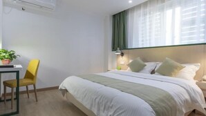 Habitación de hotel con cama, escritorio, silla, planta en maceta y ventana con cortinas.