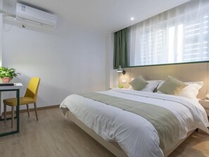 Habitación de hotel con cama, escritorio, silla, planta en maceta y ventana con cortinas.