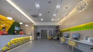 A modern hotel reception area with a yellow and white color scheme, a reception desk, seating area, and a large 'Welcome to Vatica Hotel' sign.